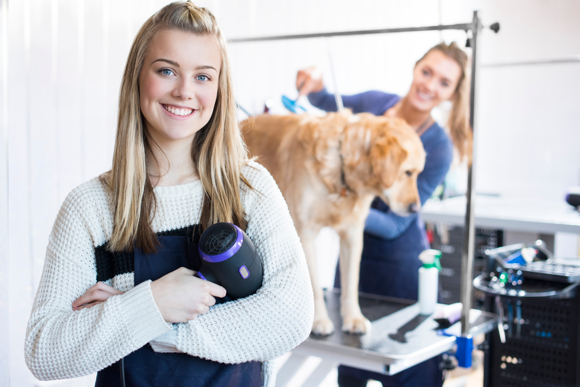 Woman packing a cardboard box, smiling. Boxes and another person nearby, in a room, light setting.
