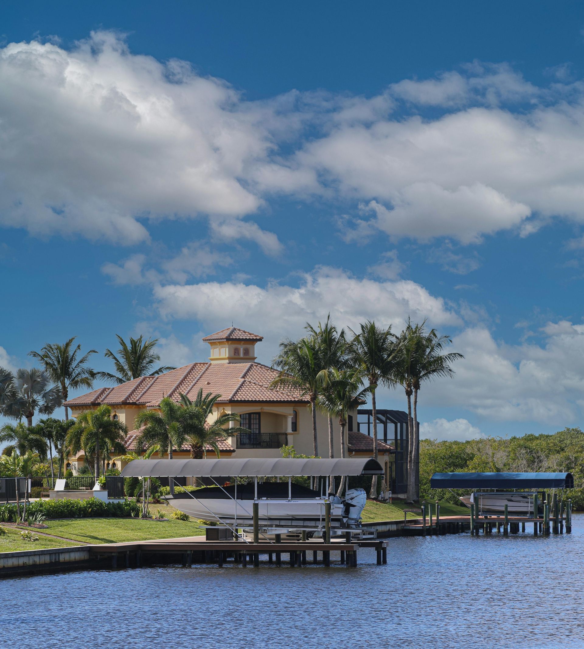 Luxury house on a waterway with a dock, sunny day, blue water, and sky with clouds.