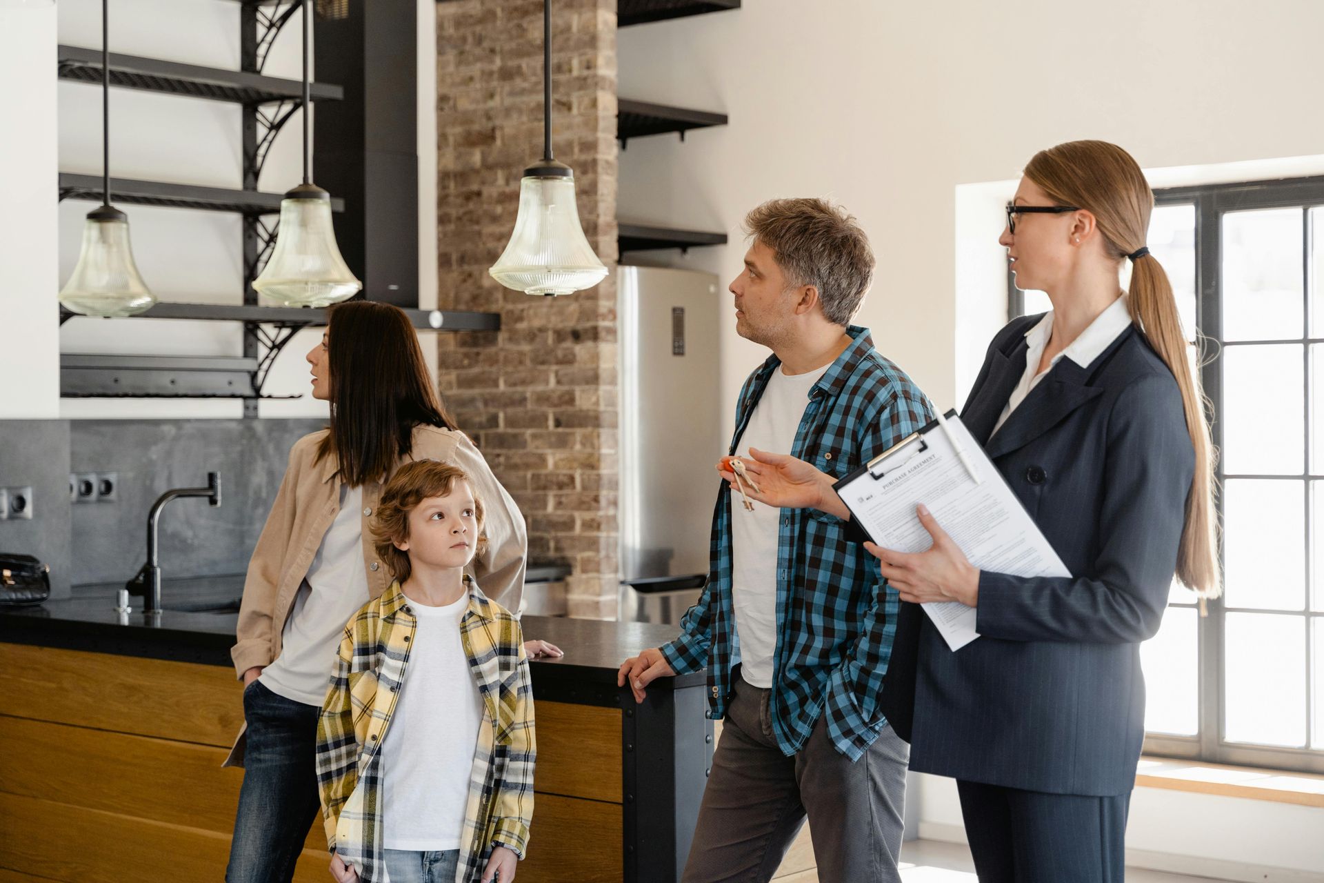 Family and realtor looking at kitchen in a house. The realtor holds a clipboard.