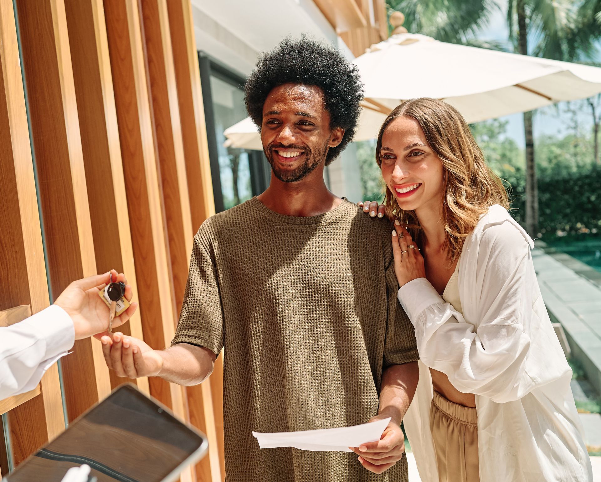 Couple smiling, receiving keys in front of modern building.