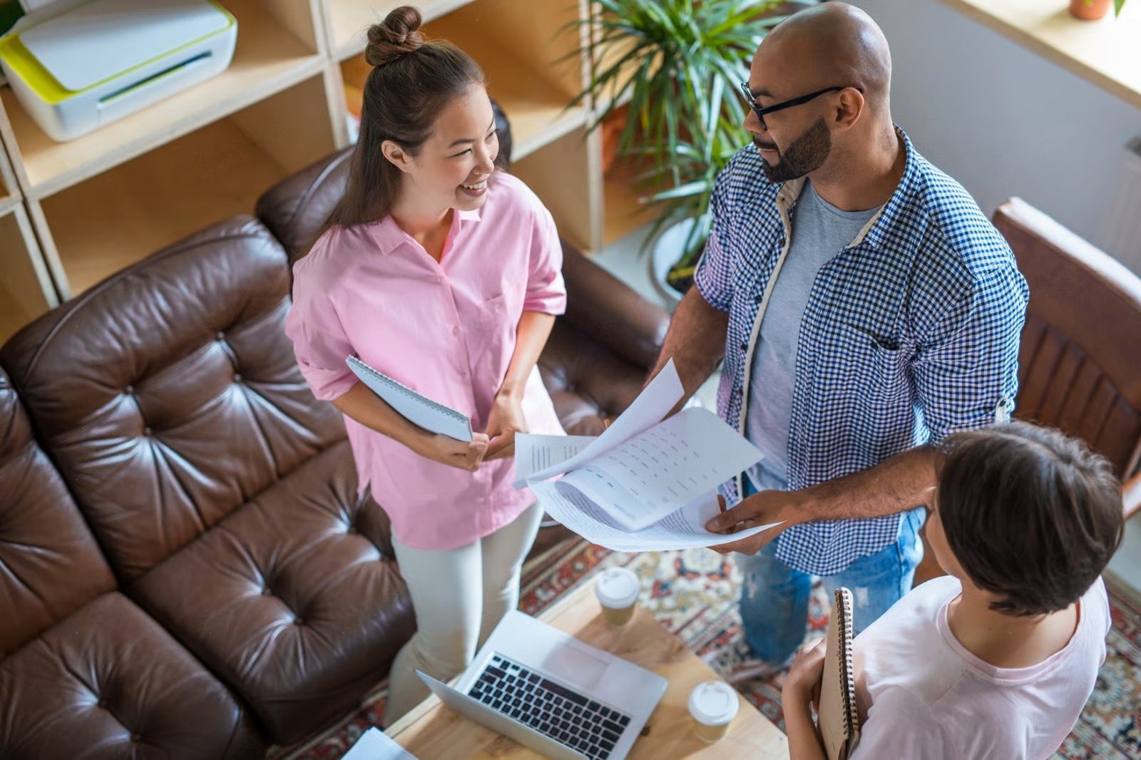 Three people reviewing documents in a living room, smiling and talking.