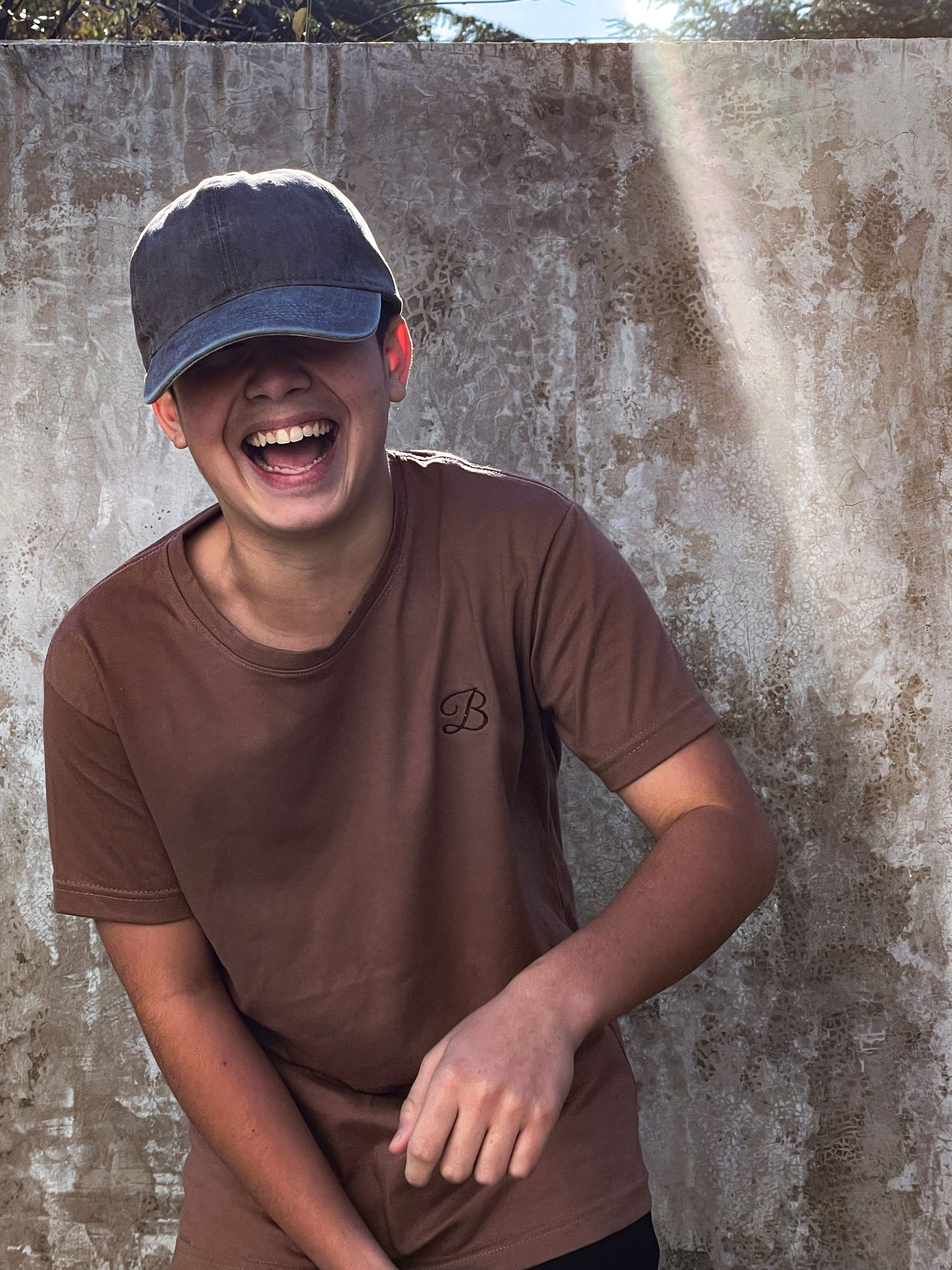 Un joven que lleva un sombrero y una camisa marrón se ríe.