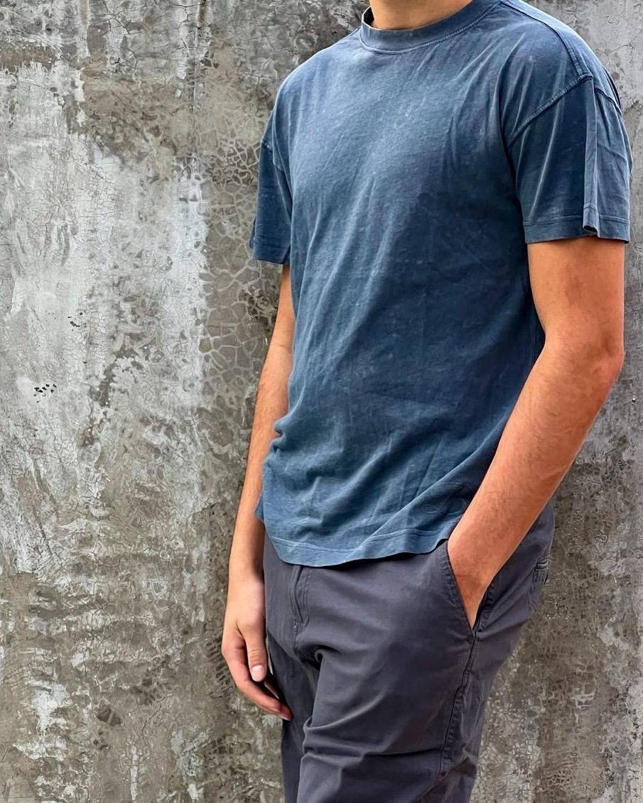 Un hombre con una camiseta azul está de pie con las manos en los bolsillos.