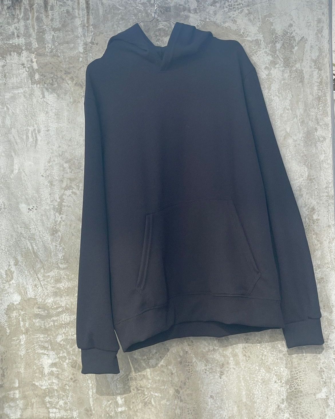 Una sudadera con capucha negra está colgada en una pared de hormigón.
