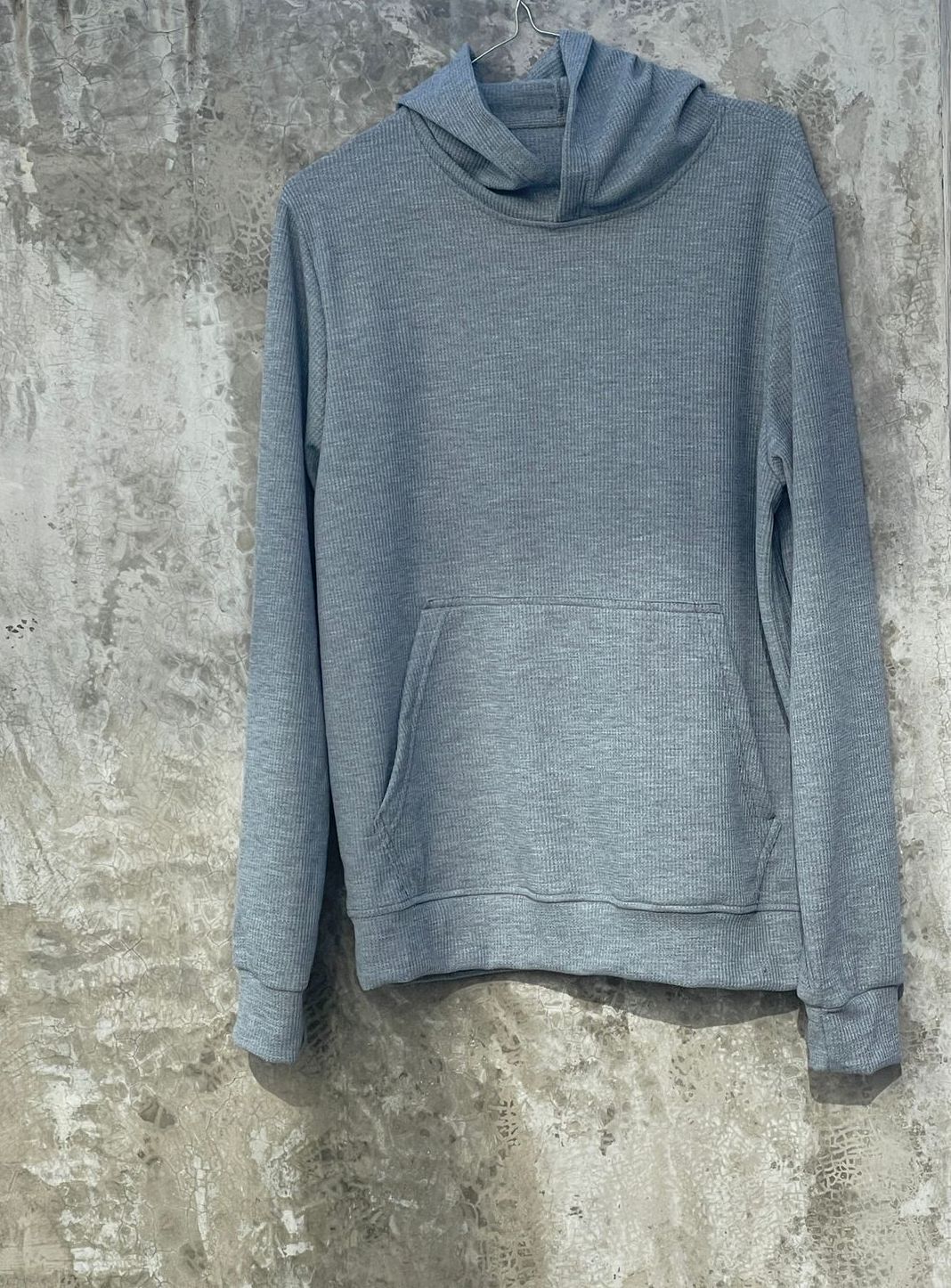 Una sudadera con capucha gris está colgada en una pared de hormigón.