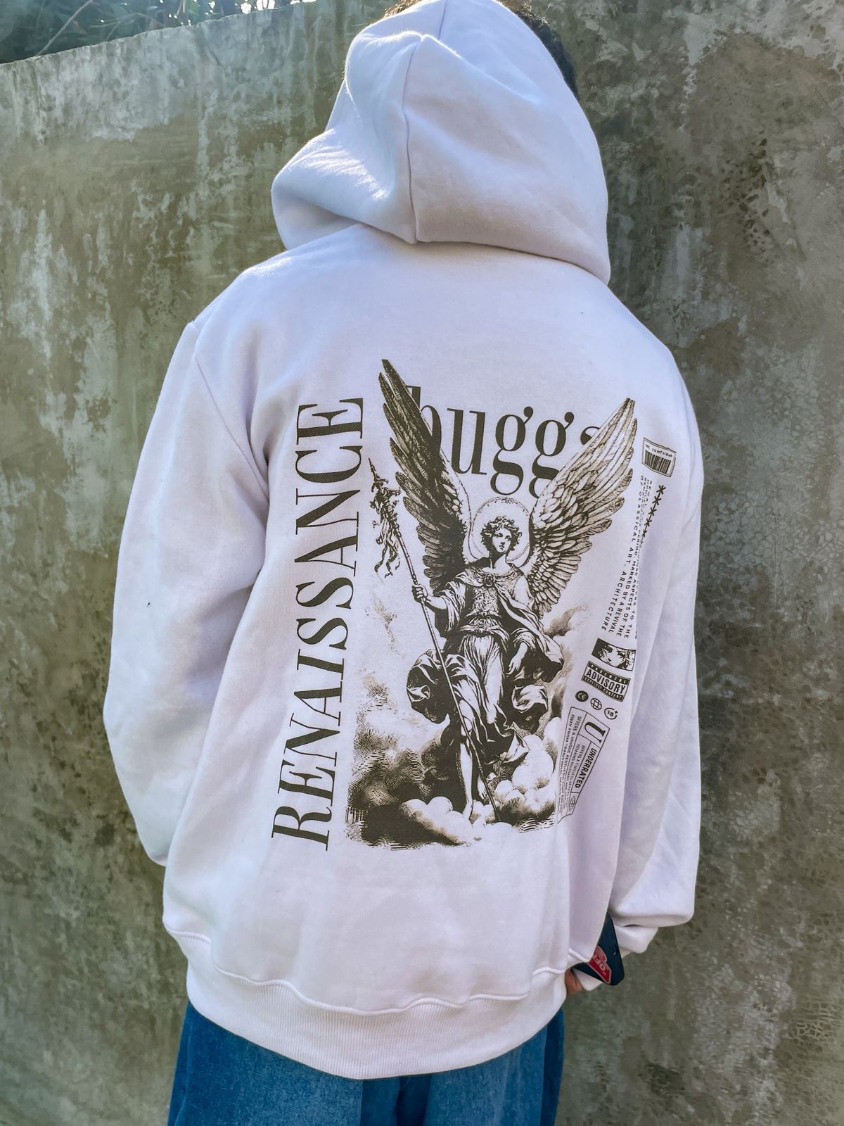 Una persona que lleva una sudadera con capucha blanca con una imagen de un ángel en la espalda.