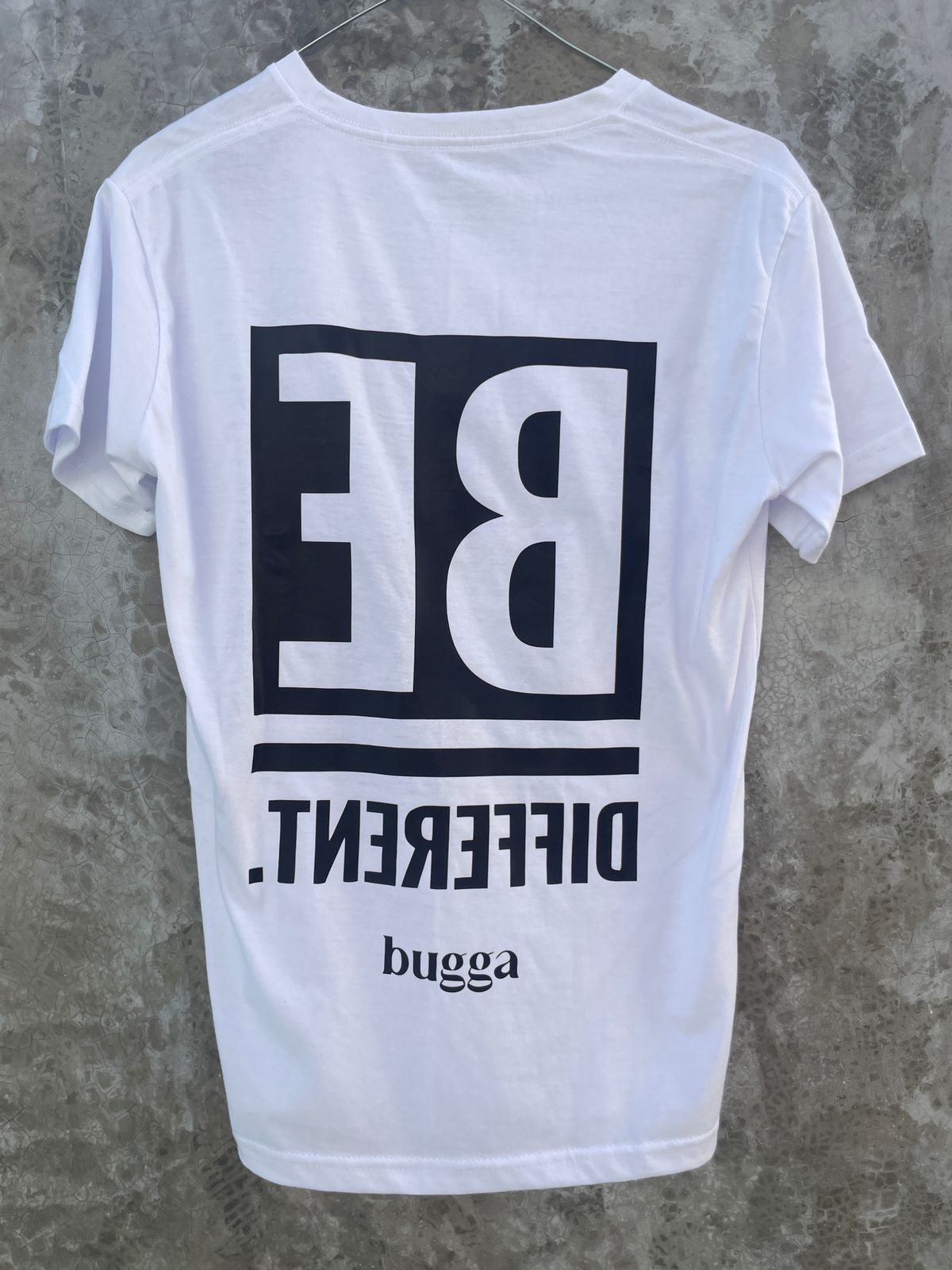 Una camiseta blanca está colgada en una percha contra una pared de hormigón.