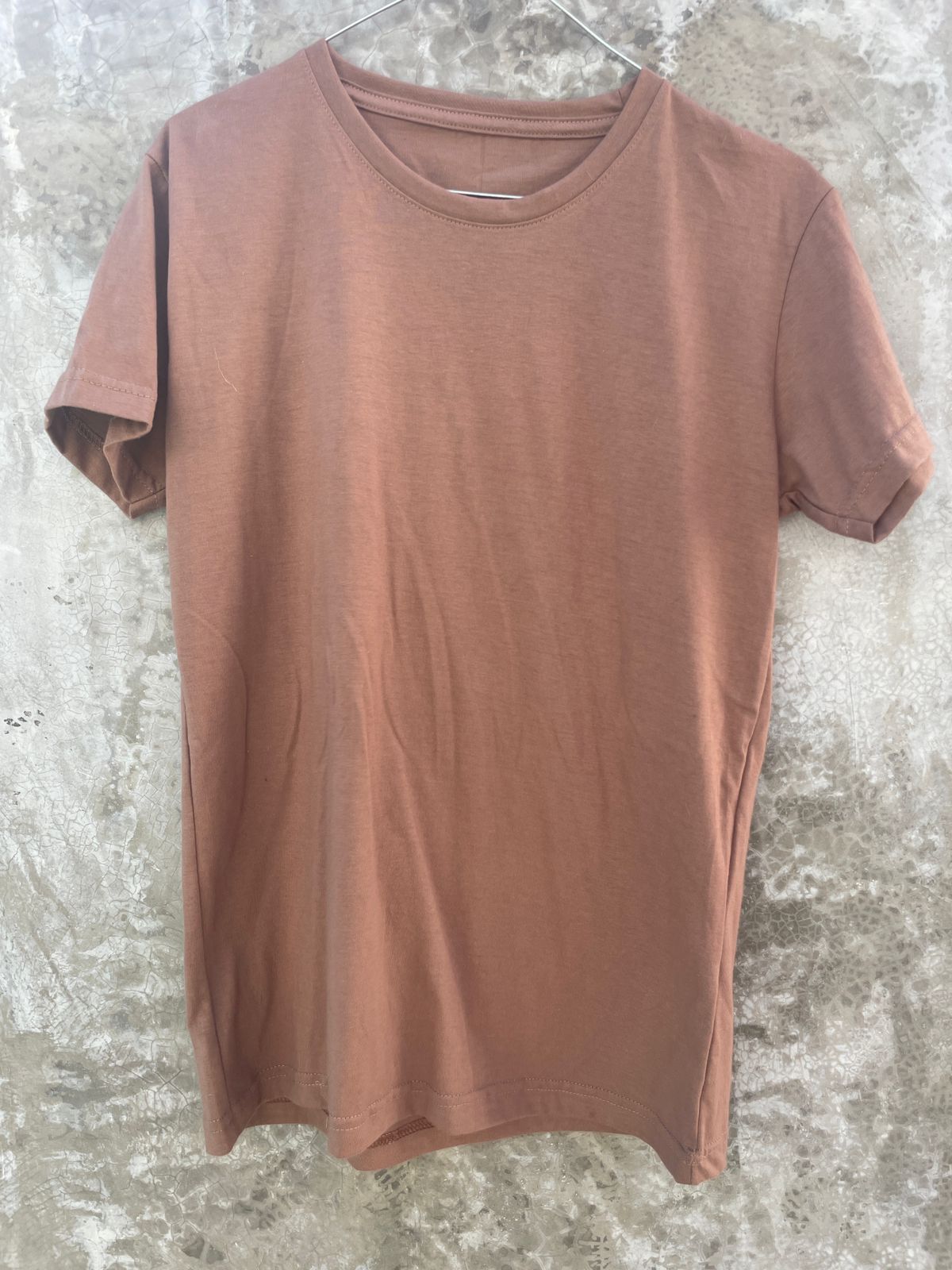 Una camiseta marrón está colgada en una pared de hormigón.