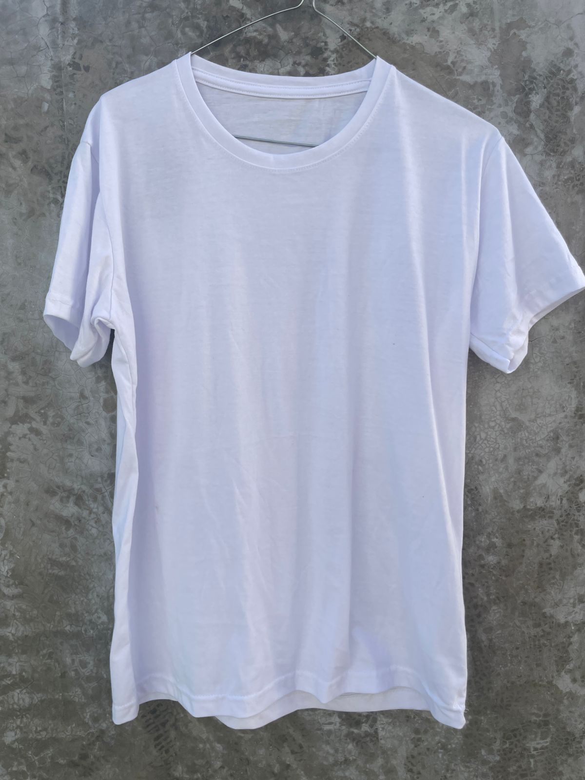 Una camiseta blanca está colgada en una percha contra una pared de hormigón.