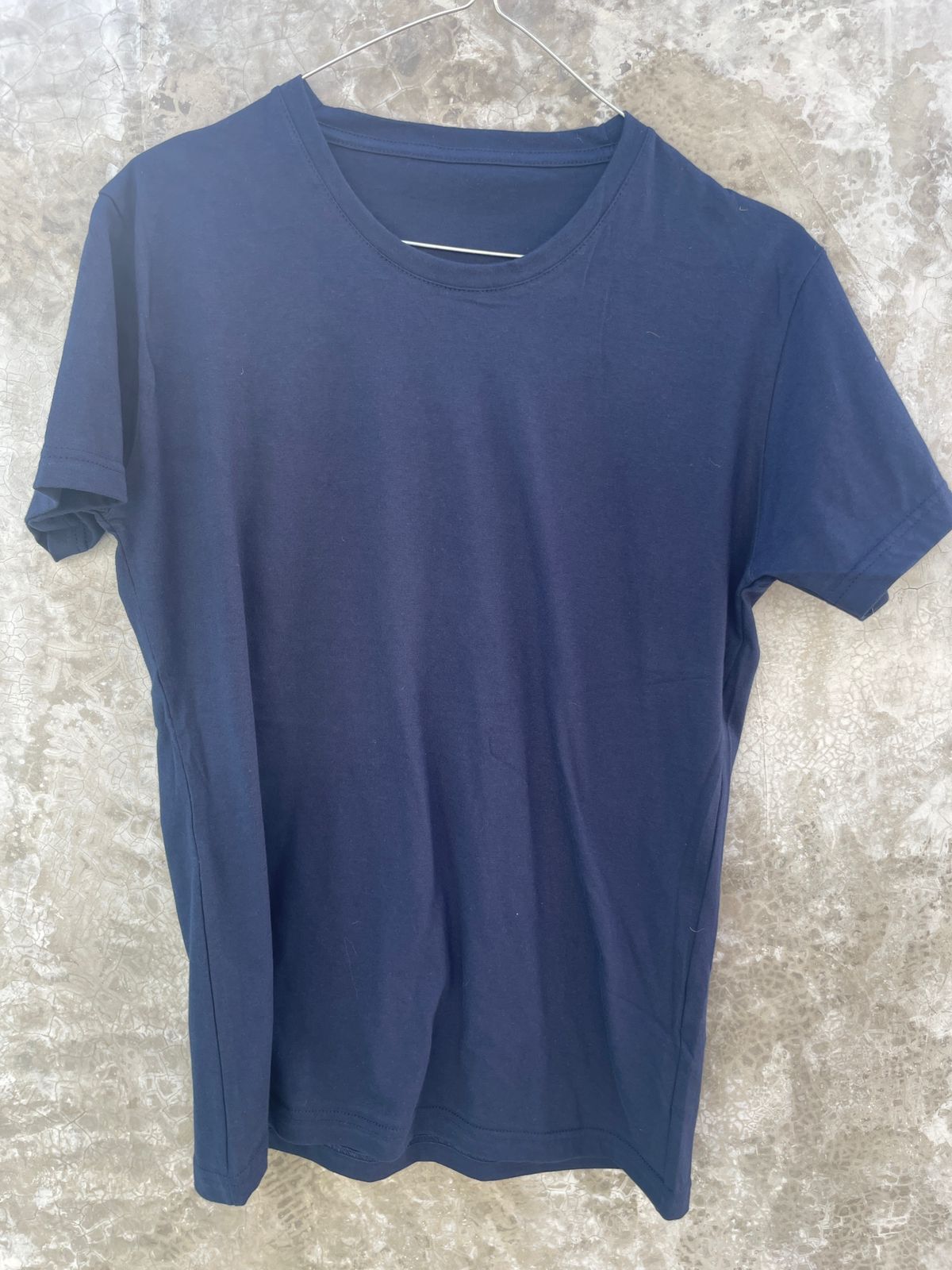 Una camiseta azul está colgada en una percha en una pared.