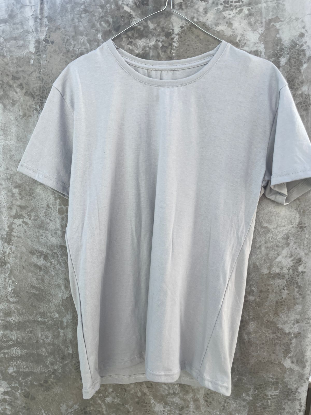 Una camiseta blanca está colgada en una percha contra una pared de hormigón.