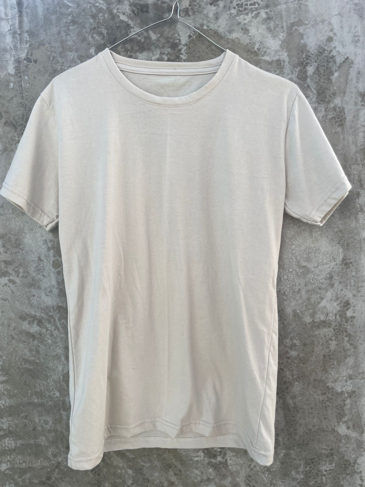 Una camiseta blanca está colgada en una percha contra una pared de hormigón.