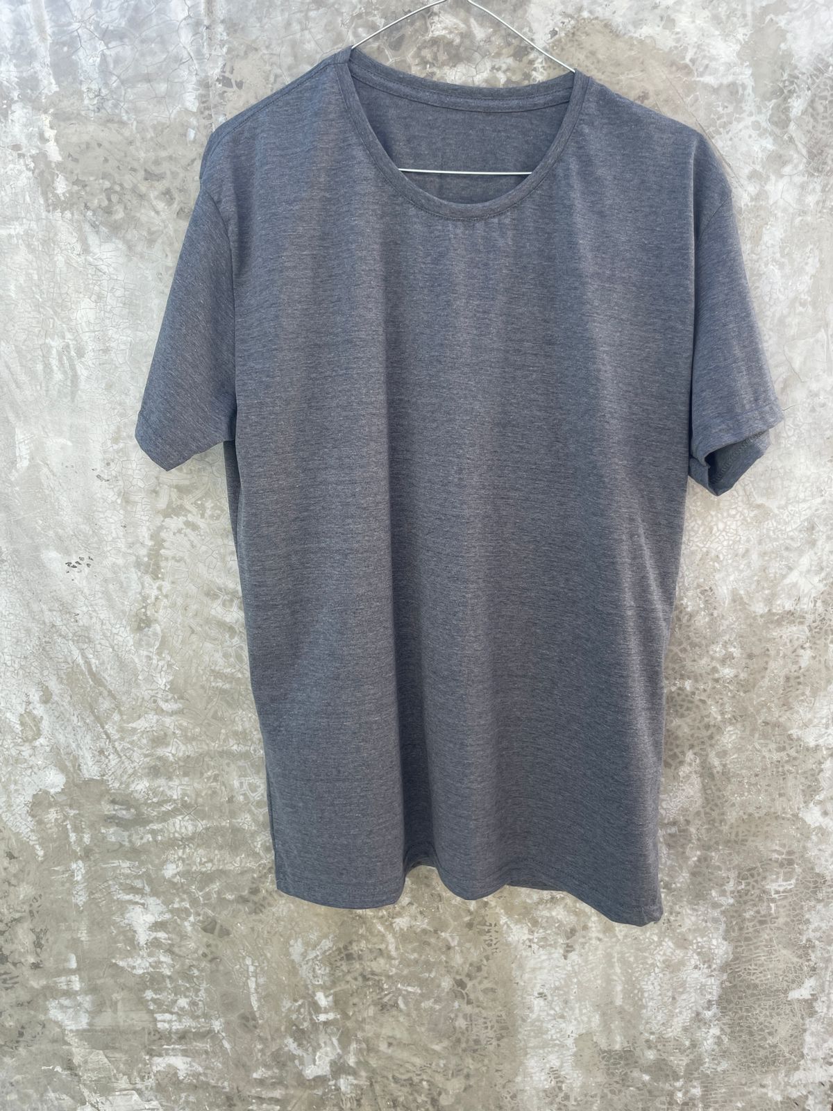 Una camiseta gris está colgada en una percha contra una pared de hormigón.