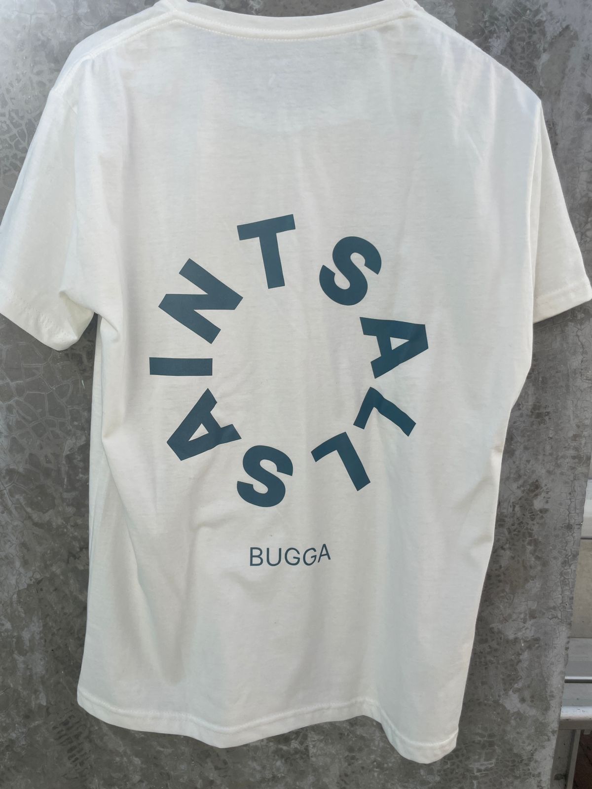 Una camiseta blanca está colgada en una percha contra una pared de hormigón.