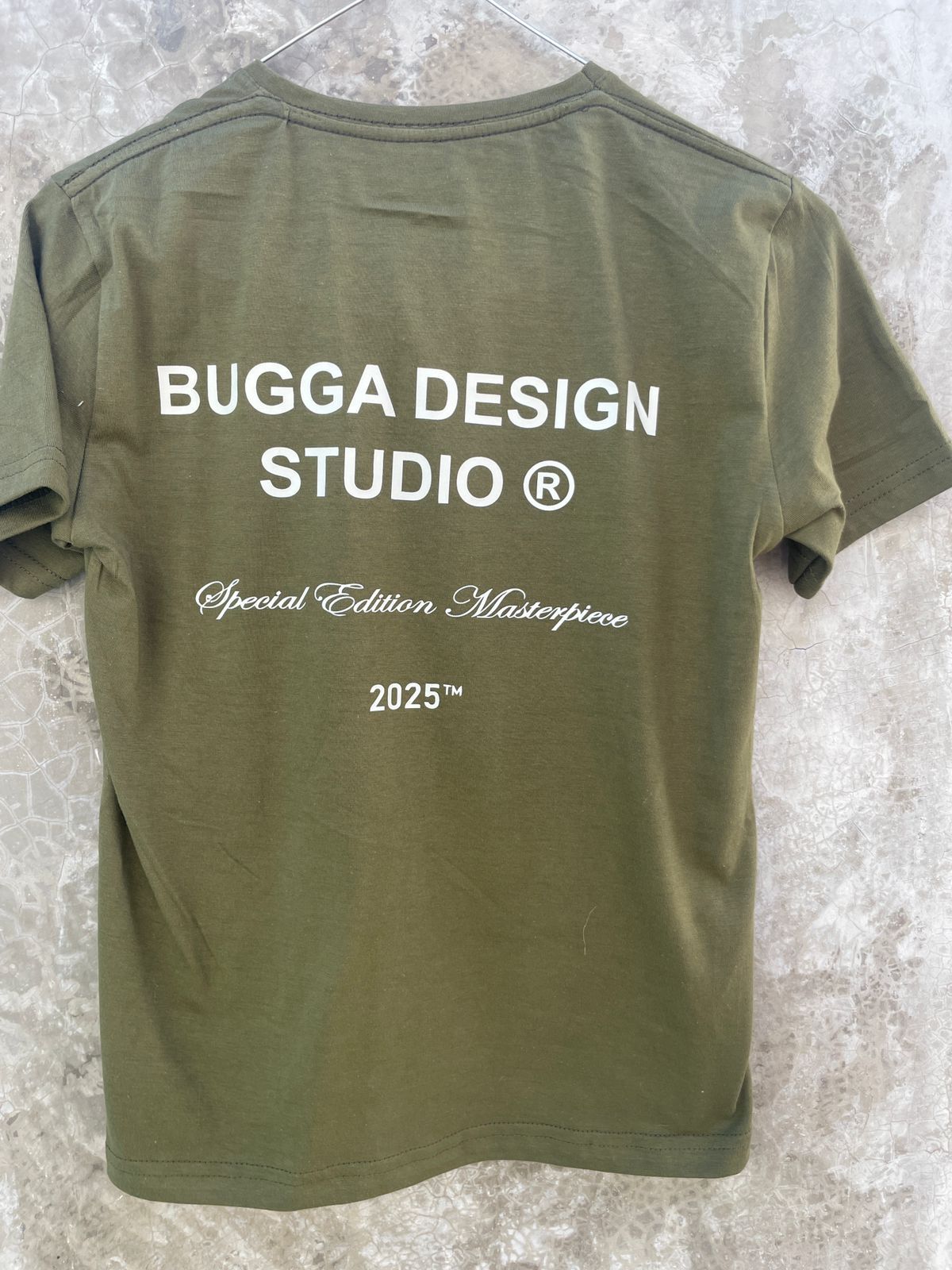 Se muestra la parte trasera de una camiseta verde de Bugga Design Studio.