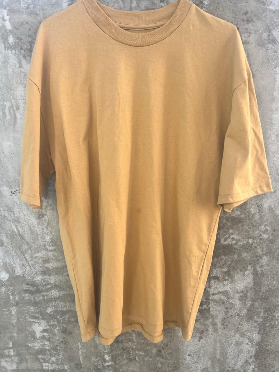 Una camiseta amarilla está colgada en una pared de hormigón.