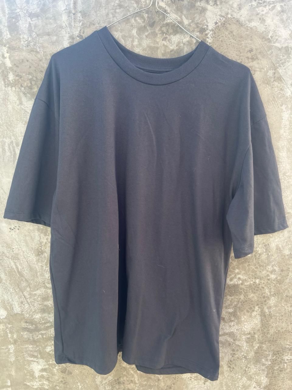 Una camiseta negra está colgada en una percha en una pared.