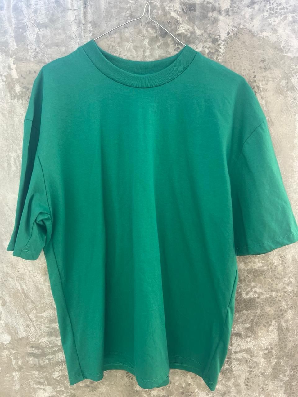 Una camiseta verde está colgada en una percha en una pared.