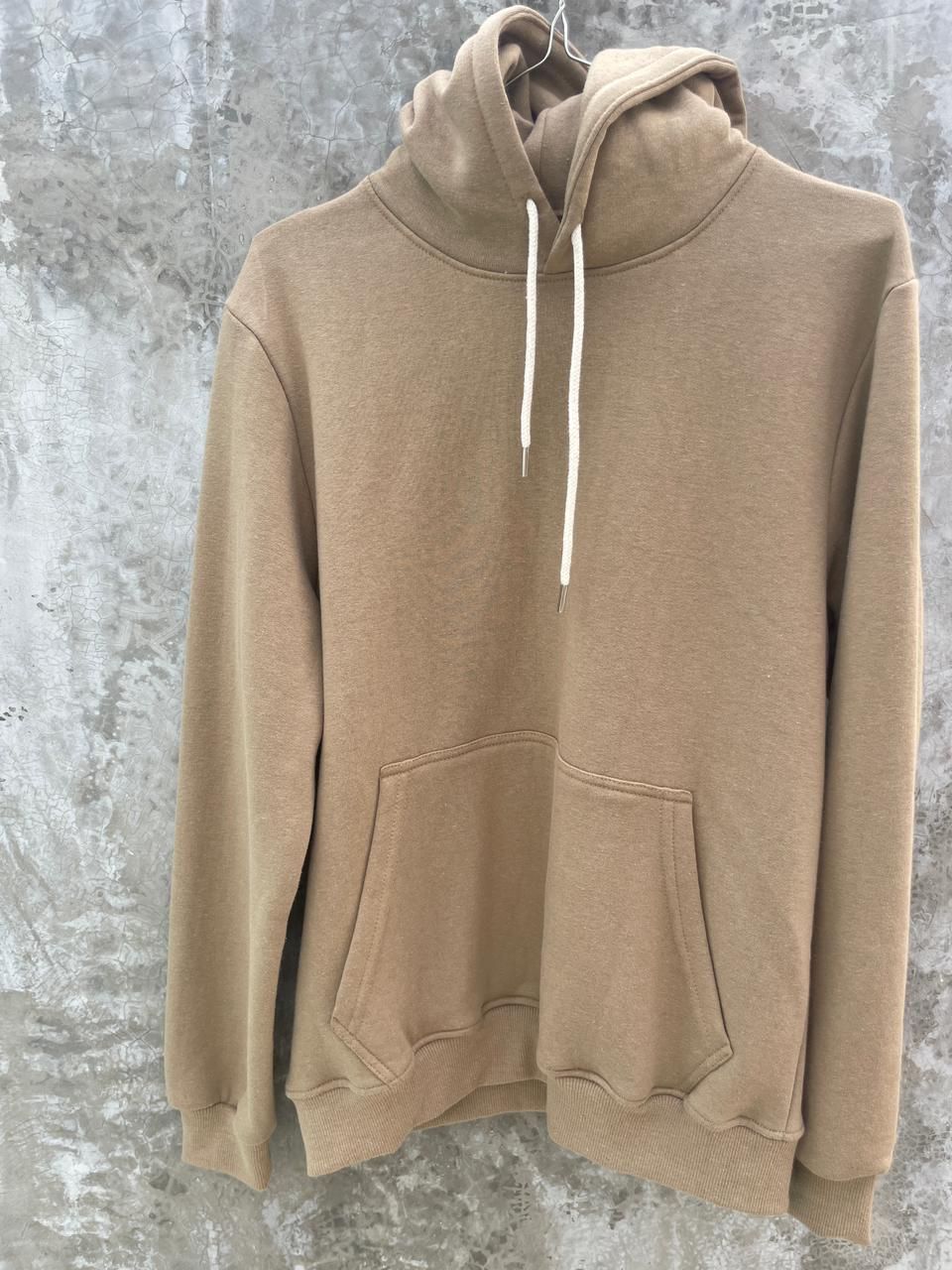Una sudadera con capucha de color marrón está colgada en una percha en la pared.