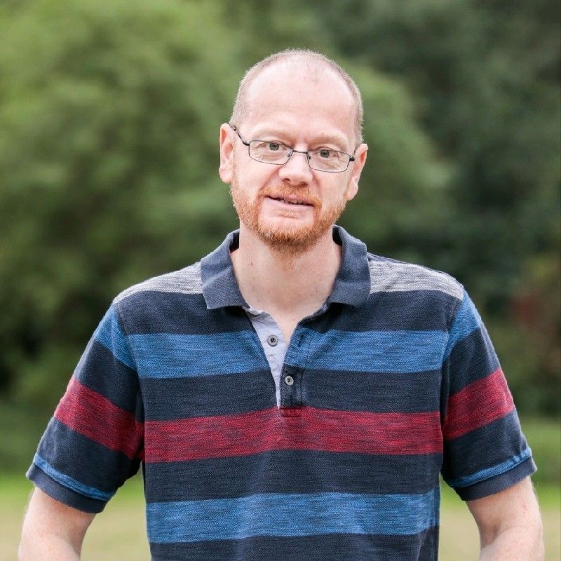 A man wearing glasses and a striped shirt is standing in a field.