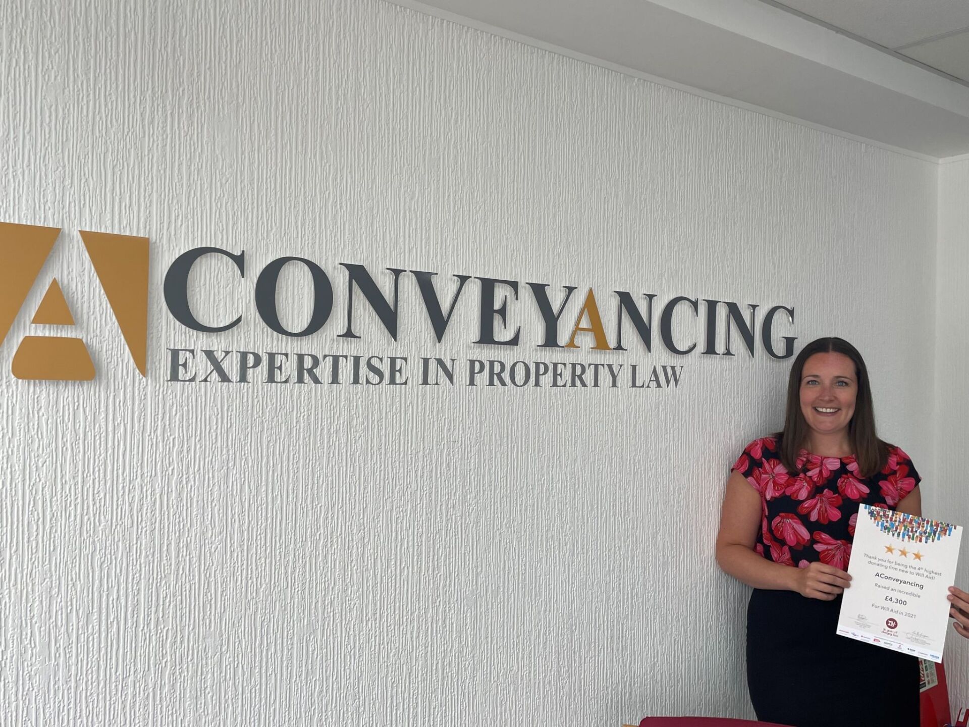 A woman is standing in front of a conveyancing sign holding a certificate.