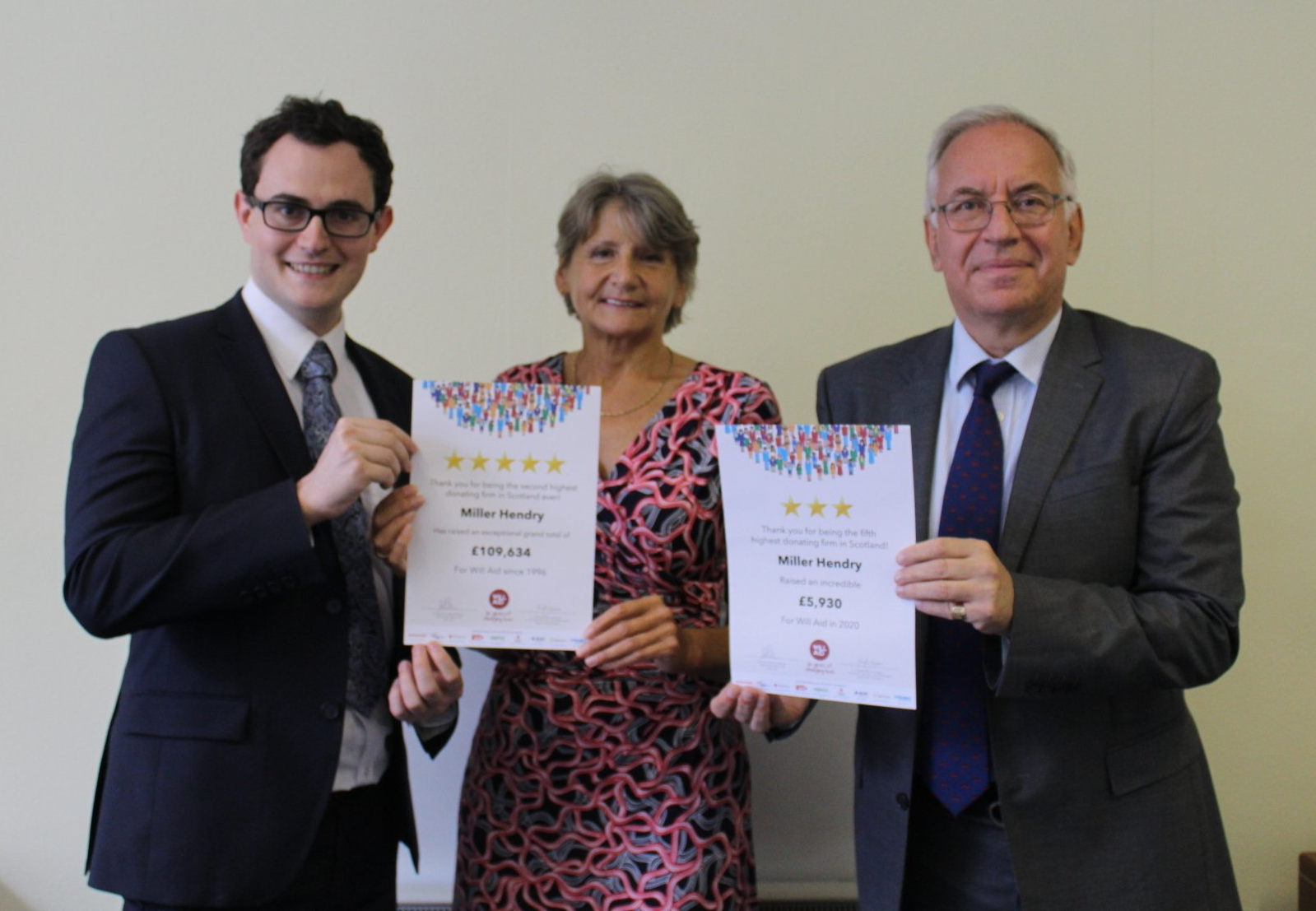 Three people in suits and ties are holding up certificates.