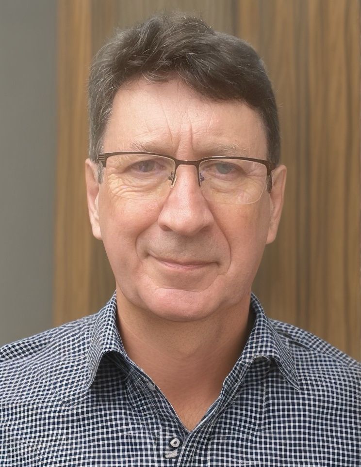 A man wearing glasses and a plaid shirt is smiling for the camera.