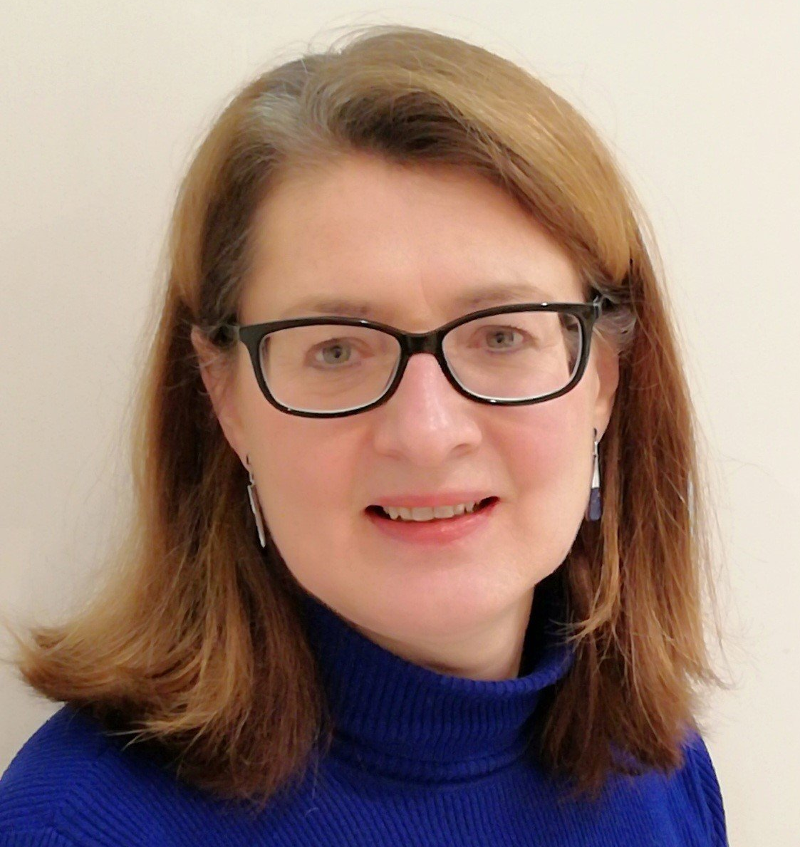 A woman wearing glasses and a blue sweater smiles for the camera