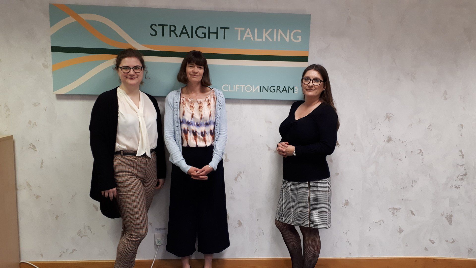 Three women are standing in front of a sign that says straight talking.