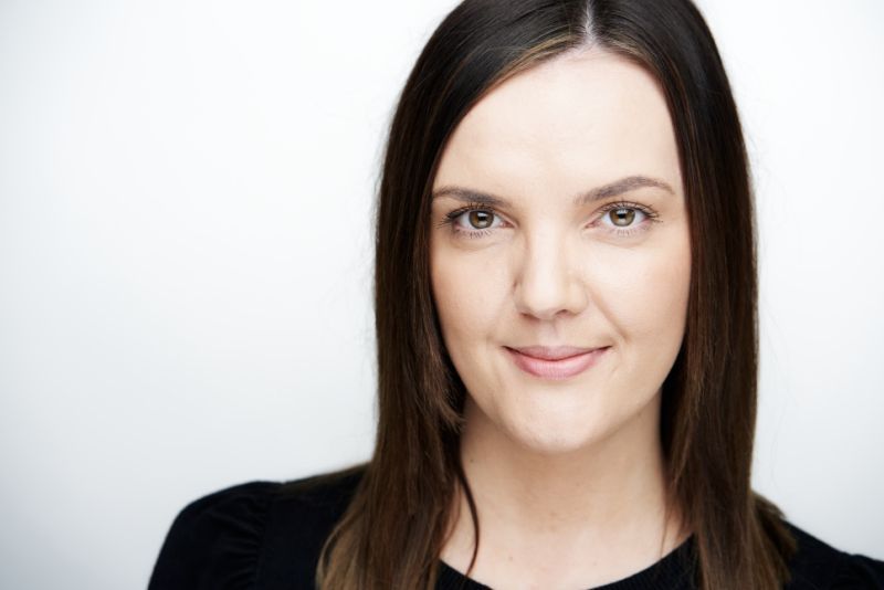 A woman with long brown hair is smiling and wearing a black shirt.