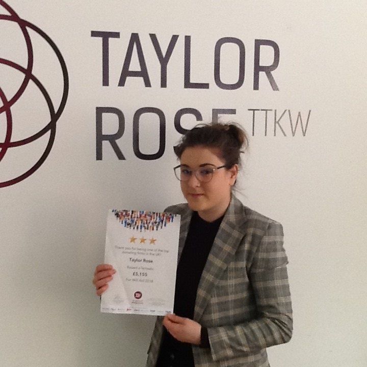 A woman is holding a certificate in front of a sign that says taylor rose tkw