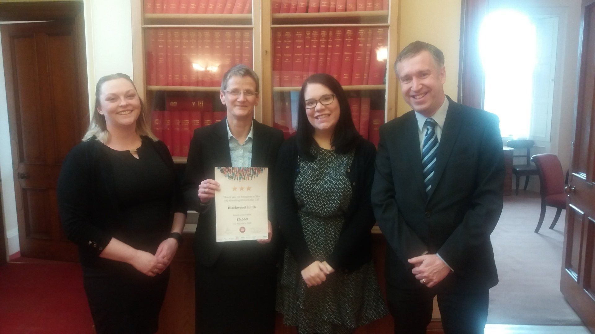 A group of people standing next to each other in front of a bookshelf holding a certificate.