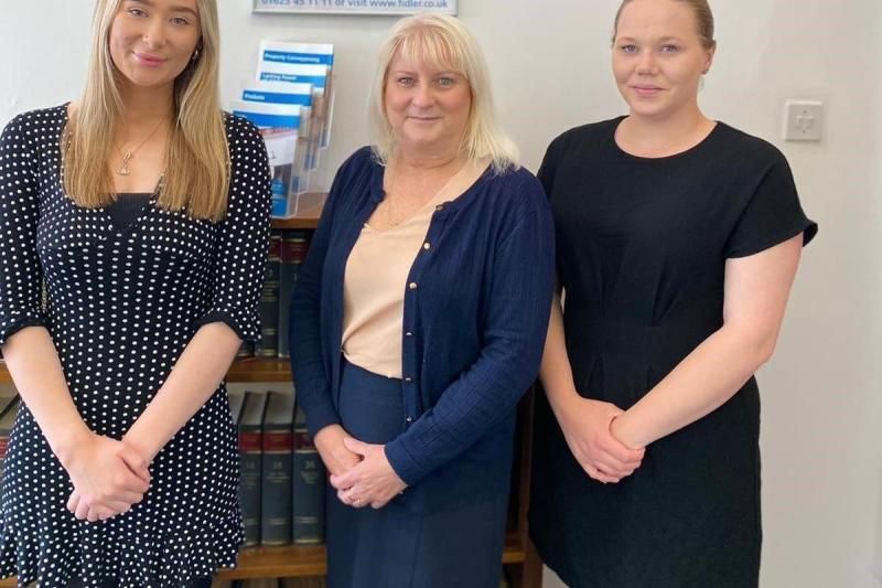 Three women are standing next to each other in front of a bookshelf.