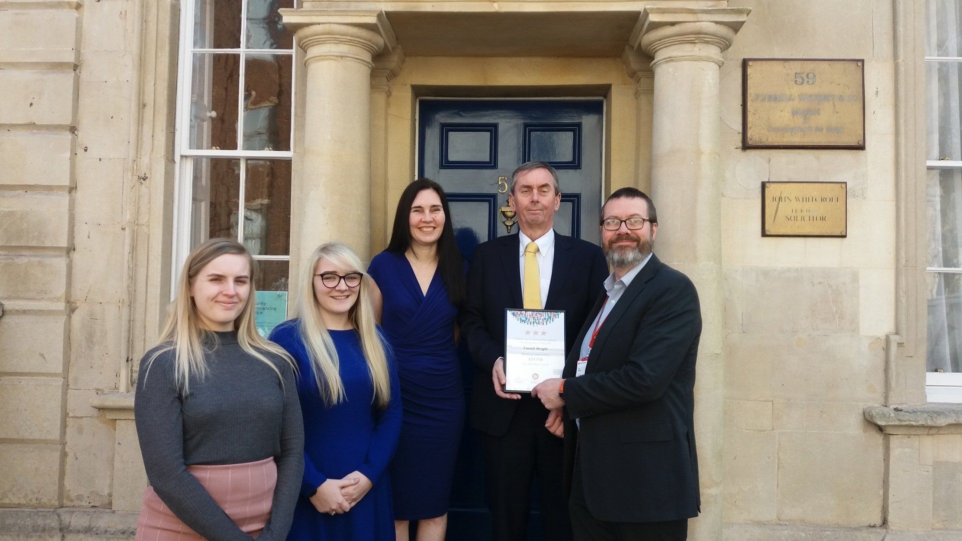 A group of people are standing in front of a building holding a certificate.