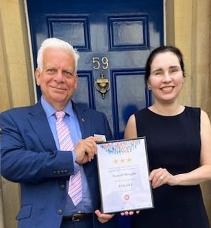 A man and a woman holding a certificate in front of a blue door with the number 59 on it