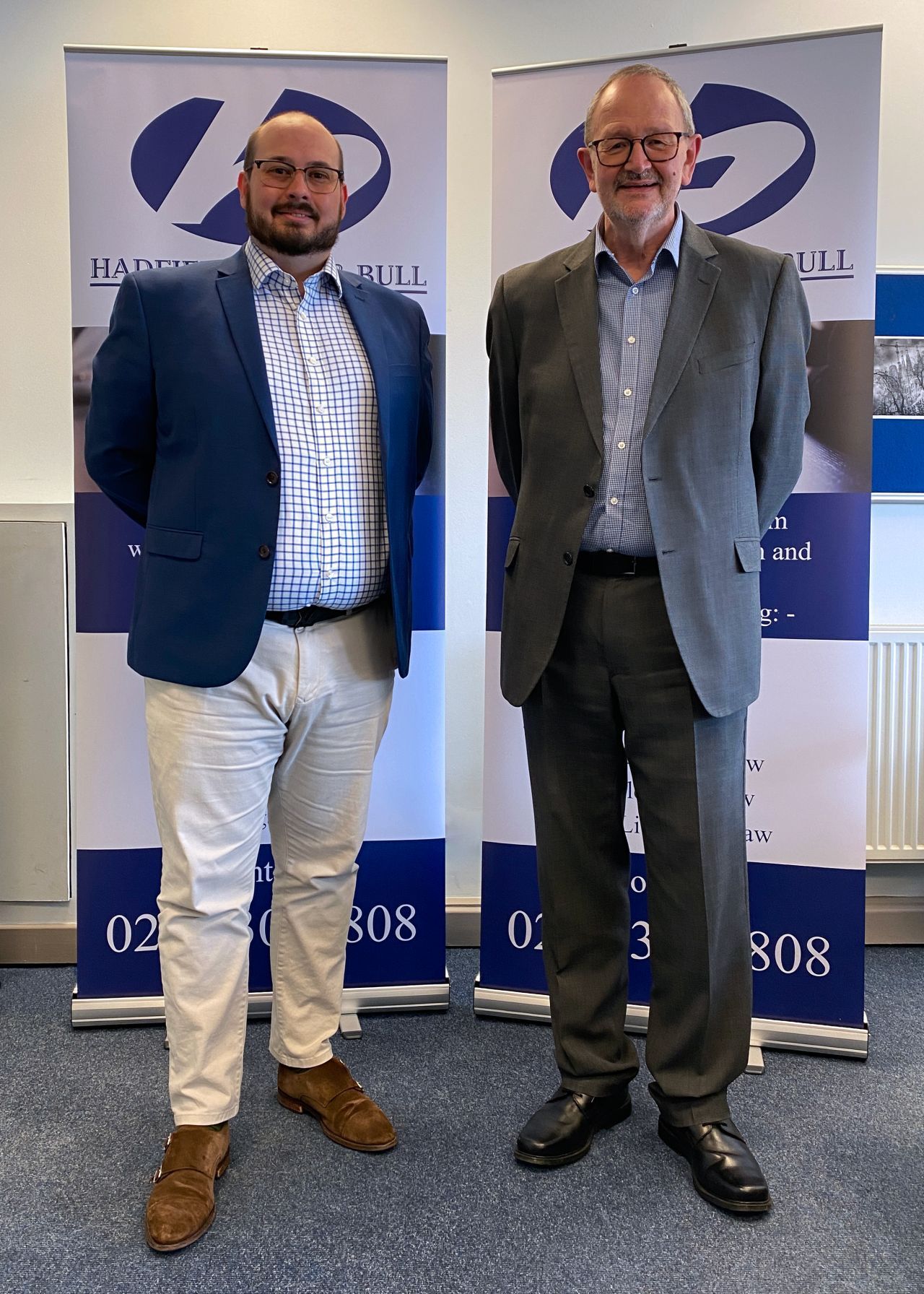 Two men in suits are standing next to each other in front of banners.