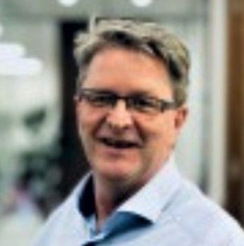 A man wearing glasses and a blue shirt is smiling for the camera.