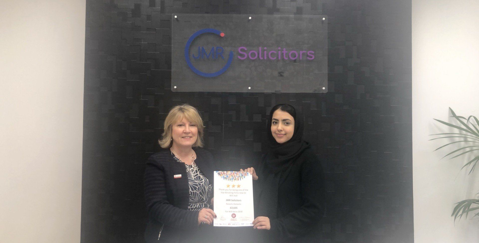 Two women are standing next to each other in front of a wall holding a certificate.