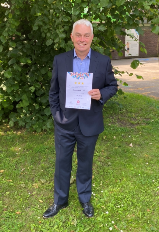 A man in a suit is standing in the grass holding a certificate.
