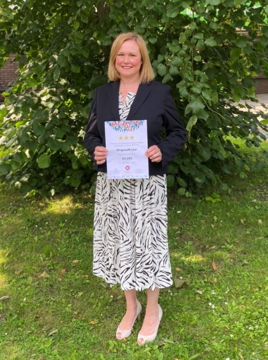 A woman is standing in the grass holding a certificate.