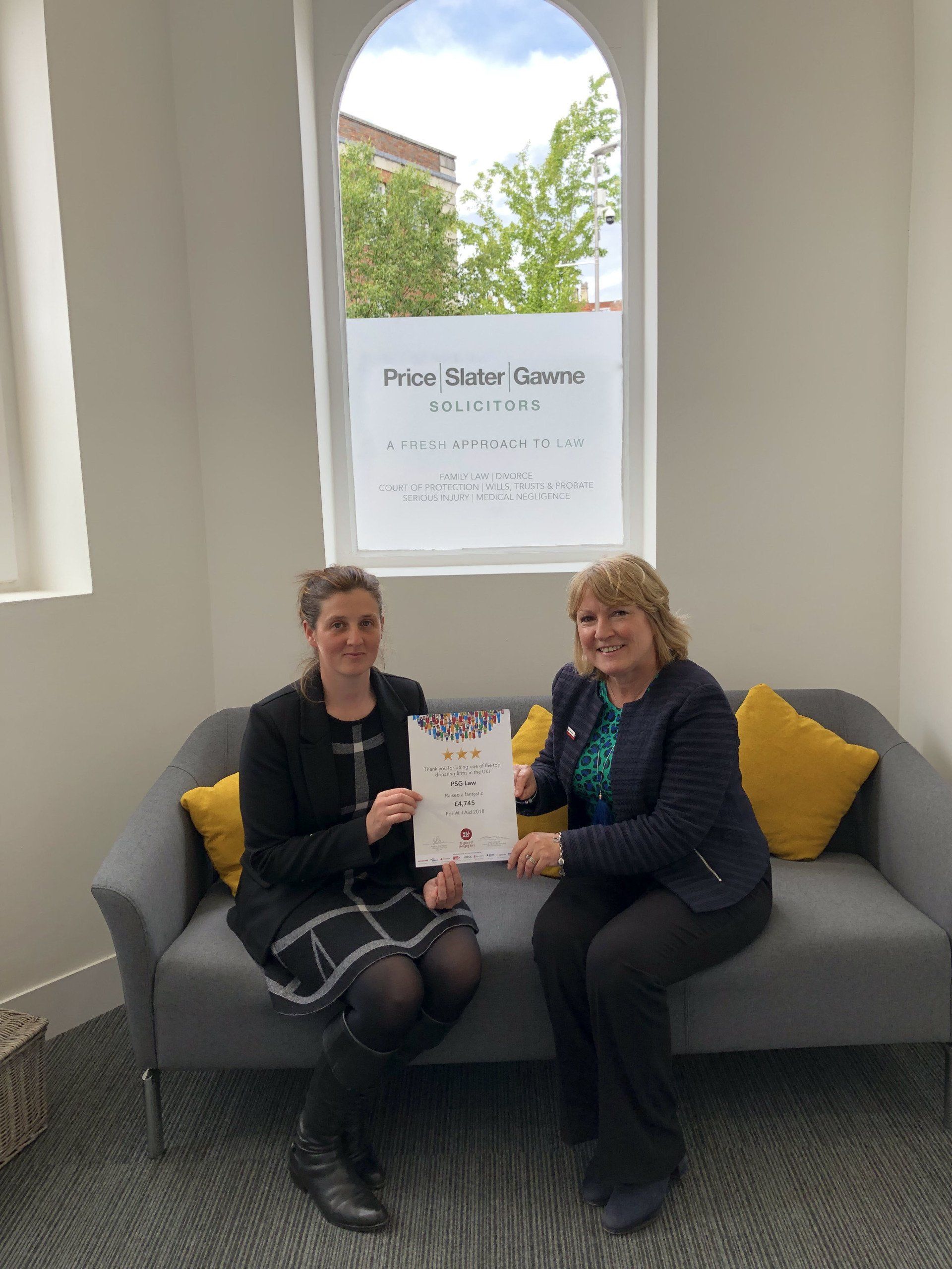 Two women are sitting on a couch holding a certificate.