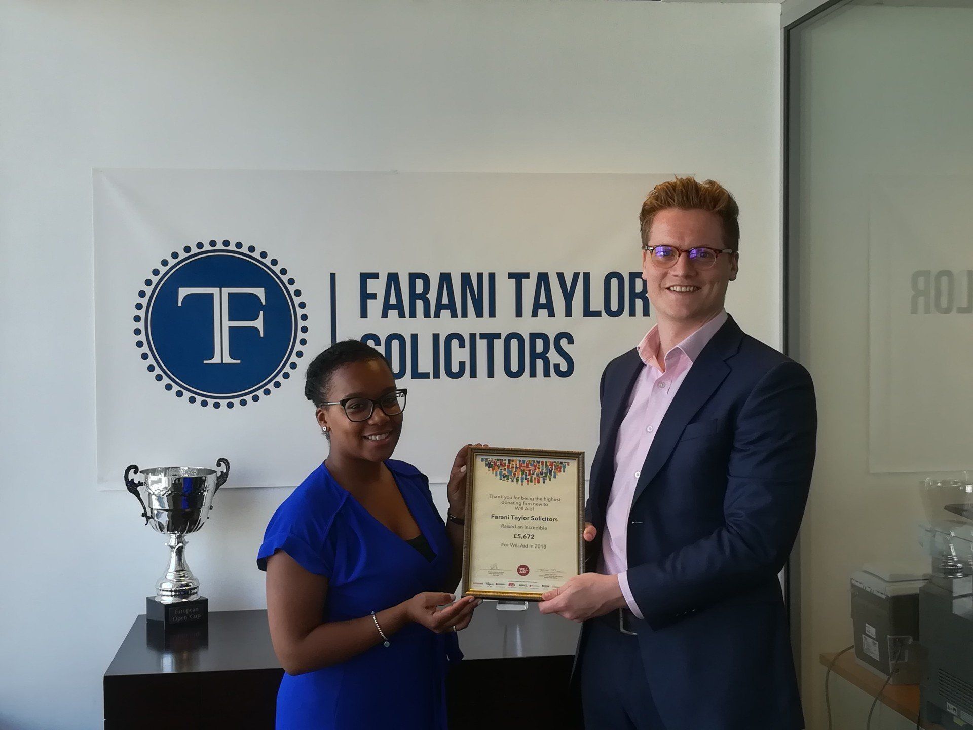 A man and a woman are standing in front of a farani taylor solicitors sign