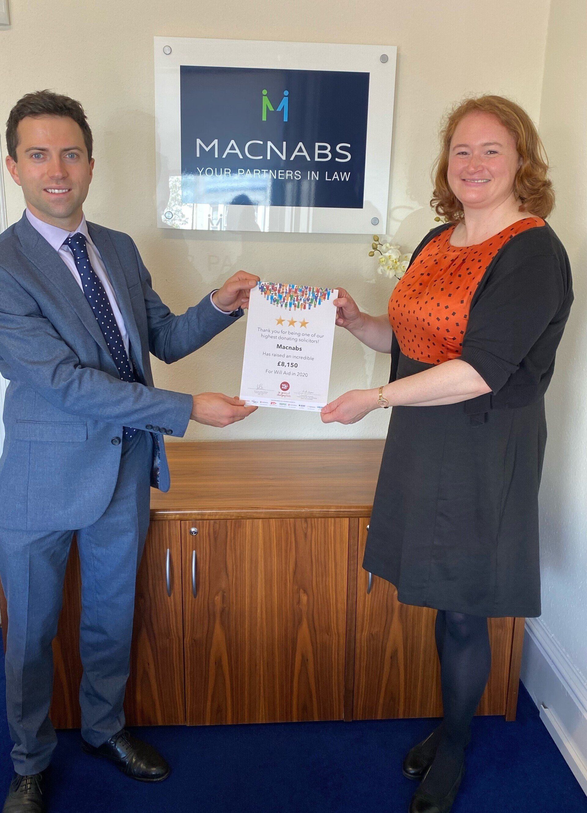 A man and a woman are standing next to each other in front of a sign that says macnabs.