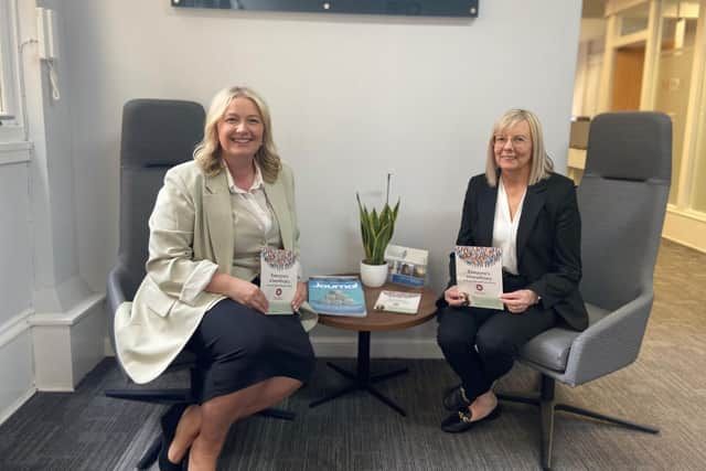 Two women are sitting in chairs in a room holding books.