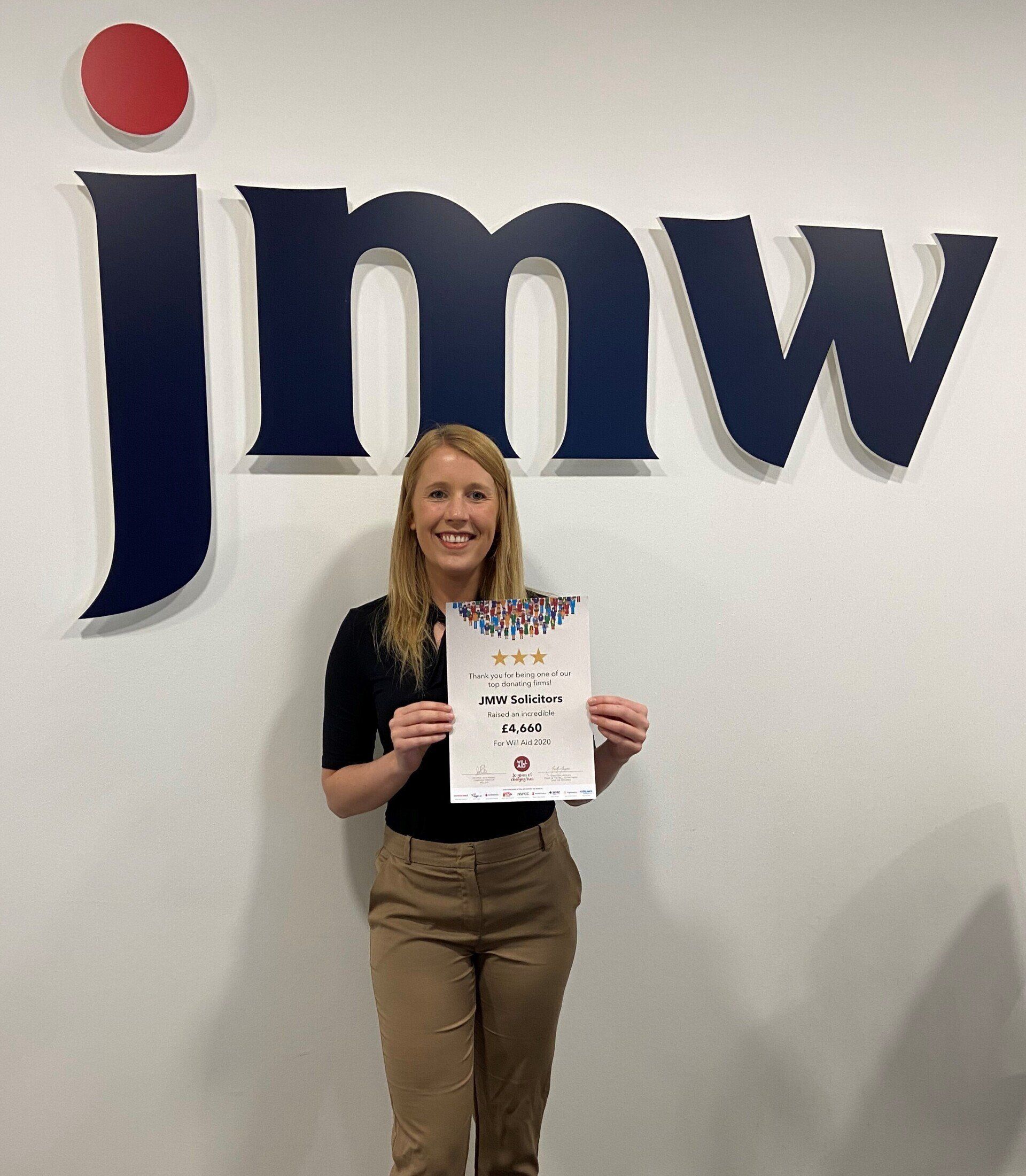 A woman is standing in front of a jimw sign holding a piece of paper.