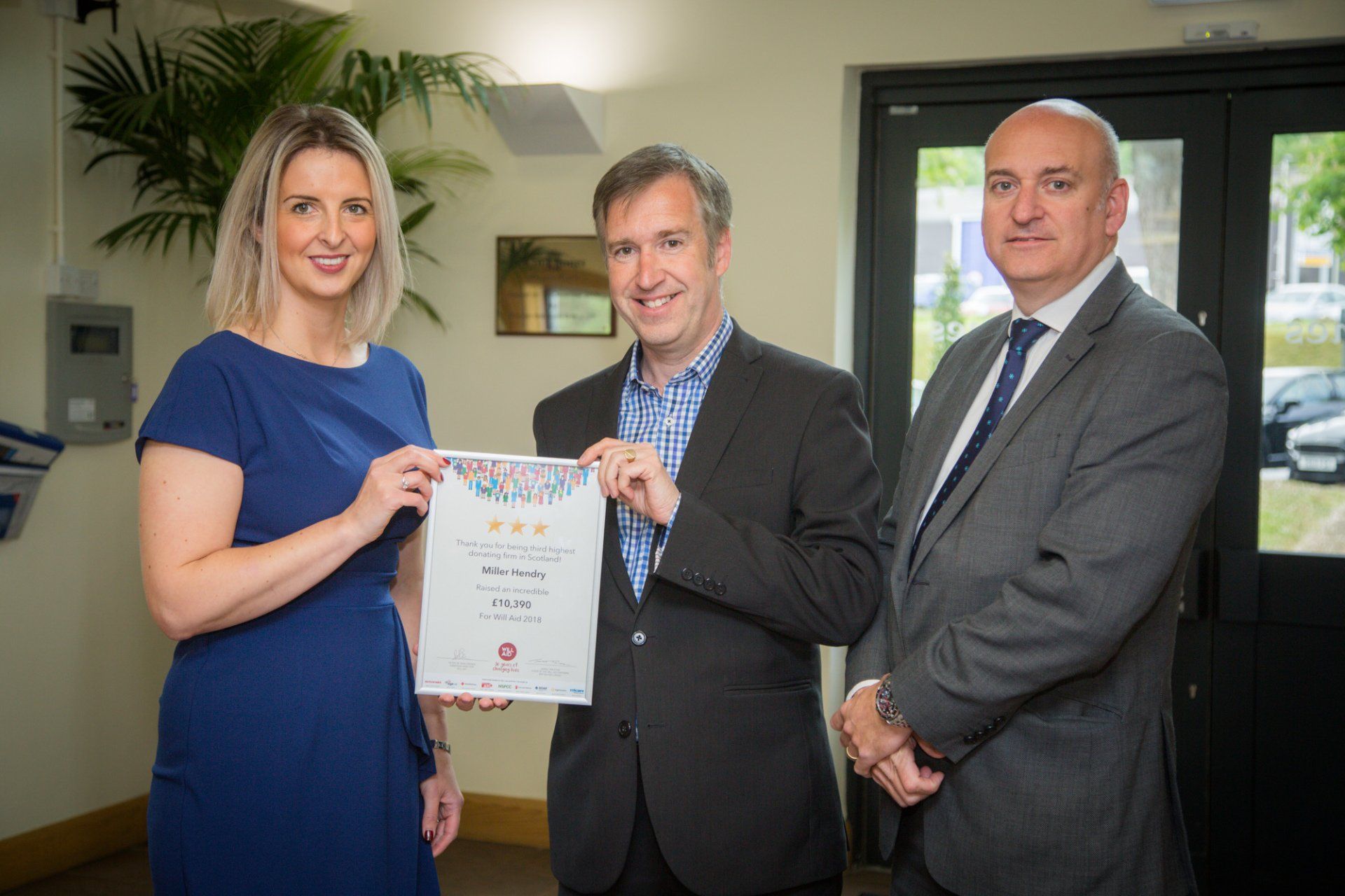 A woman is holding a certificate between two men in suits.