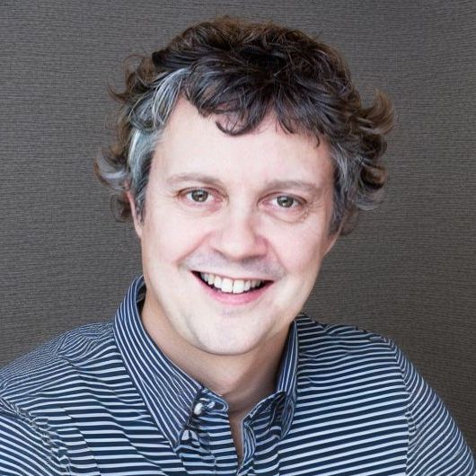 A man wearing a striped shirt is smiling for the camera