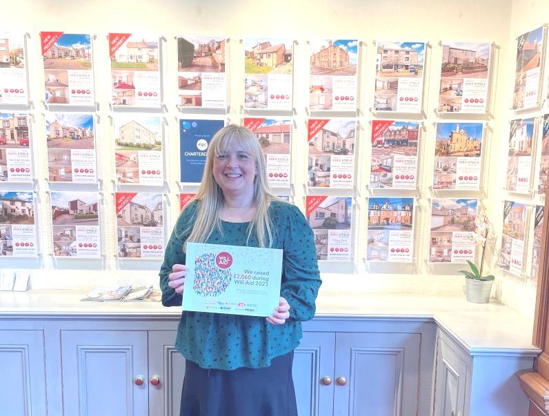 A woman is holding a sign in front of a wall of real estate brochures.