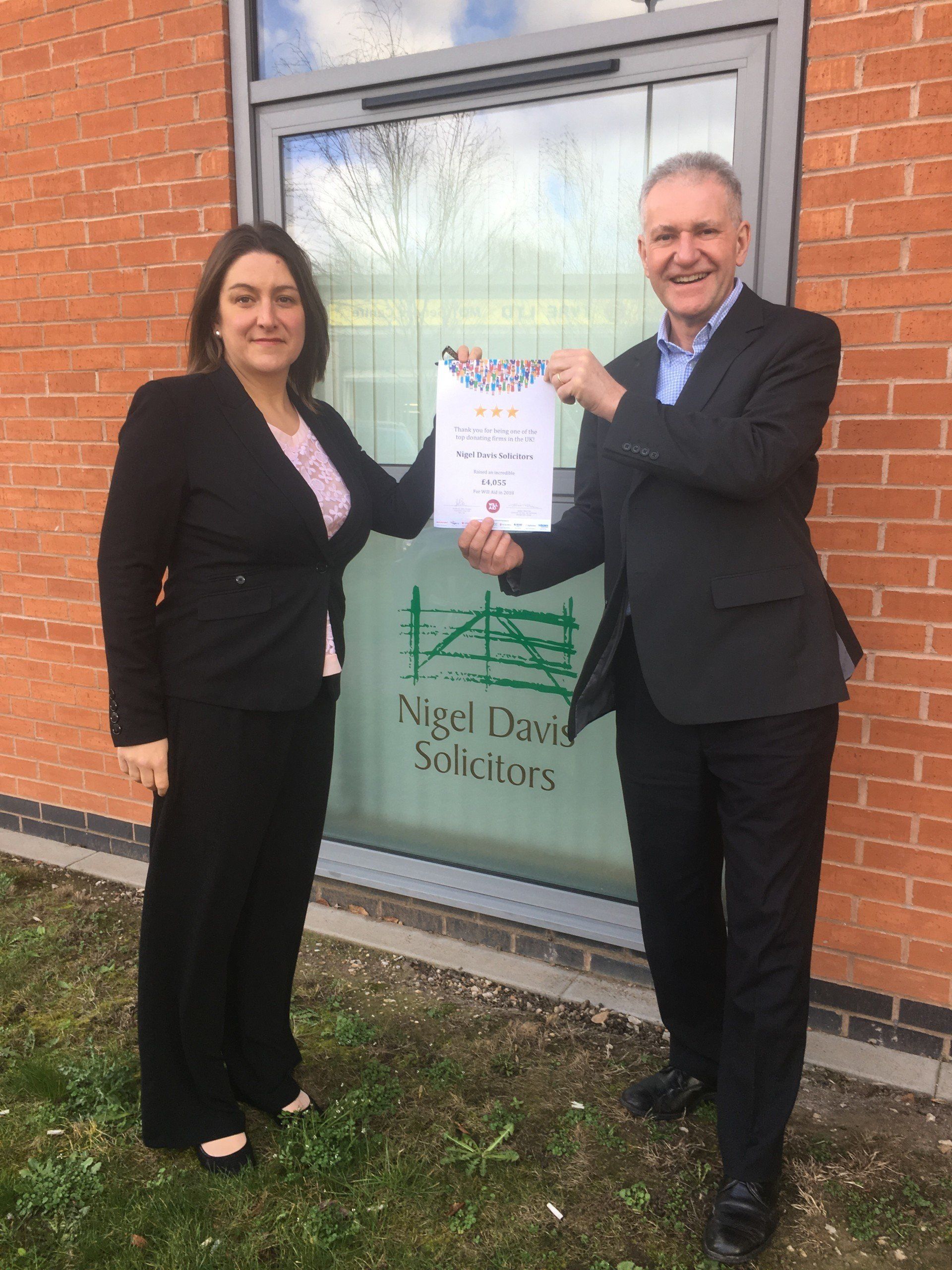 A man and a woman are shaking hands in front of a brick building.