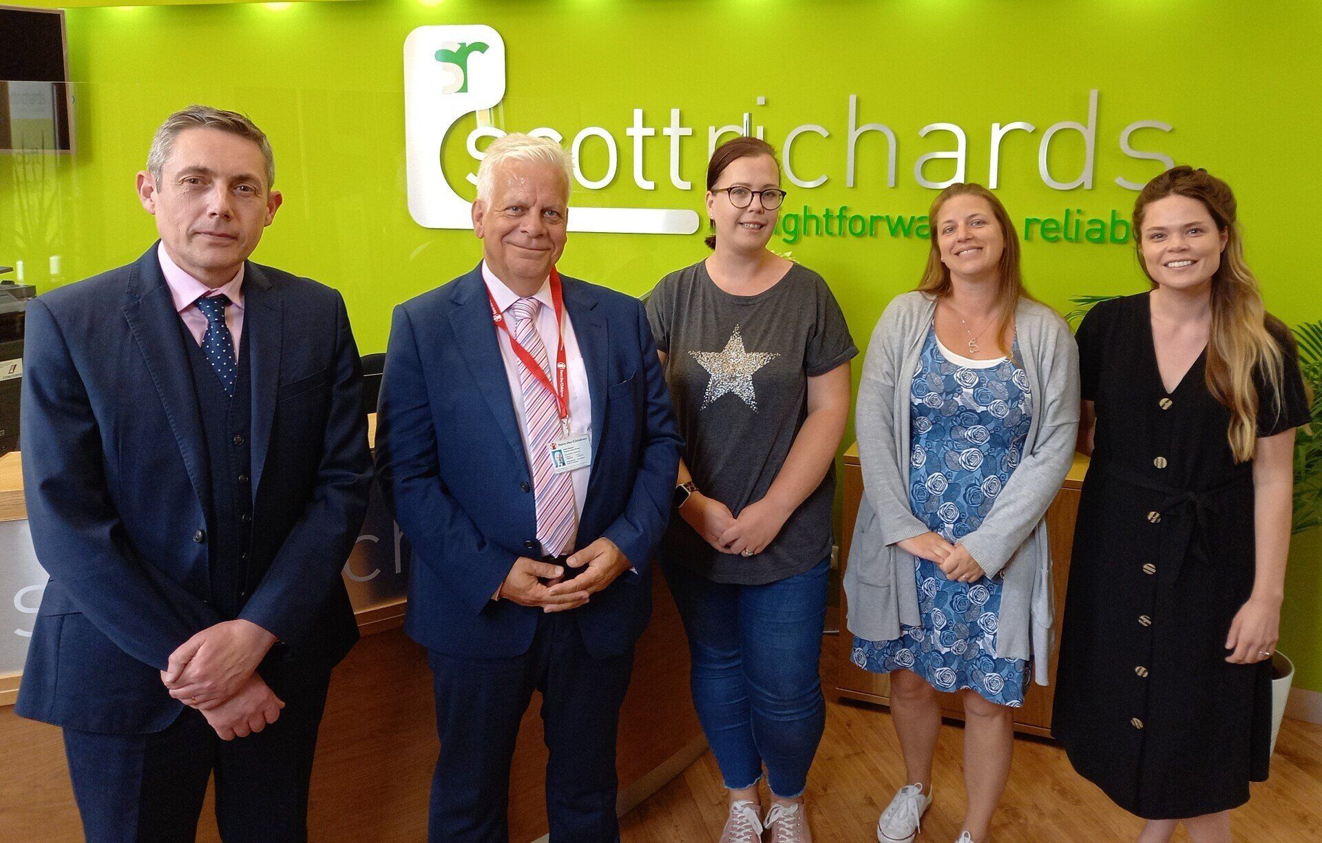 A group of people are standing in front of a green sign that says scott richards.